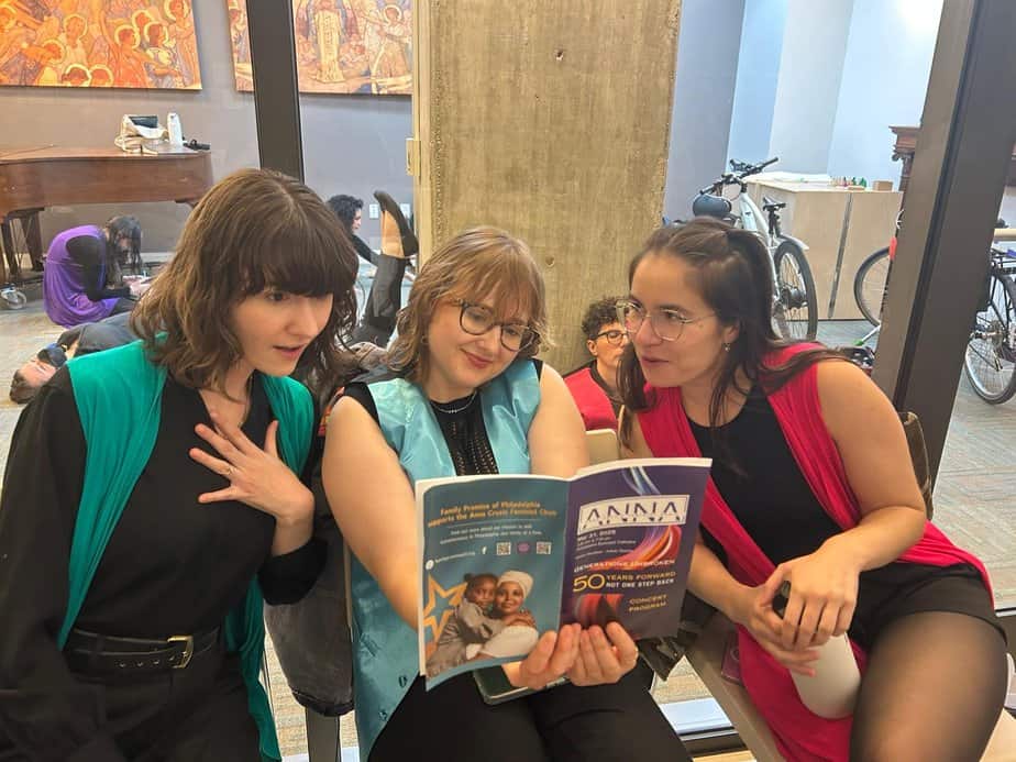 3 younger singers looking at the concert program for "generations Unbroken.